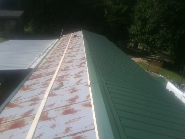 Old rusted panels beside newly installed green metal roofing — Wind Damage Roof Repair by Roofing Brothers in Craigsville