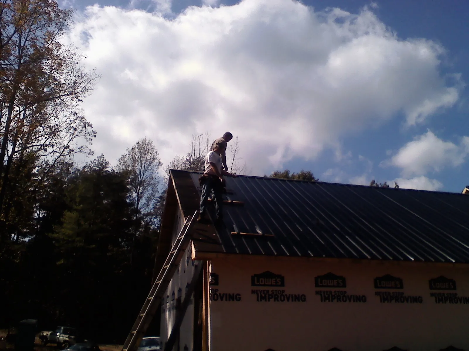 Roofer fastening dark metal panels high against a cloudy sky, from a Roof Inspection job in Craigsville